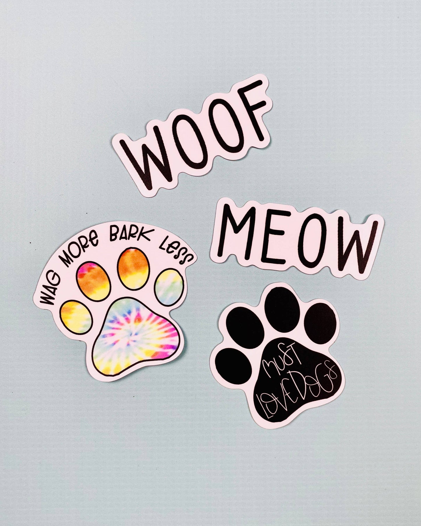 Three stickers with text and paw designs on a light gray background