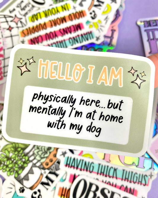 Sticker with text 'HELLO I AM physically here... but mentally I'm at home with my dog' on a colorful background.